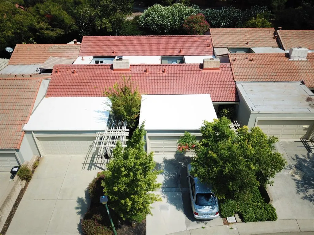 Aerial view of rooftops in Livermore, featuring a newly completed white flat roof by PRI-Premiere Roofing Inc. surrounded by traditional red-tiled roofs.